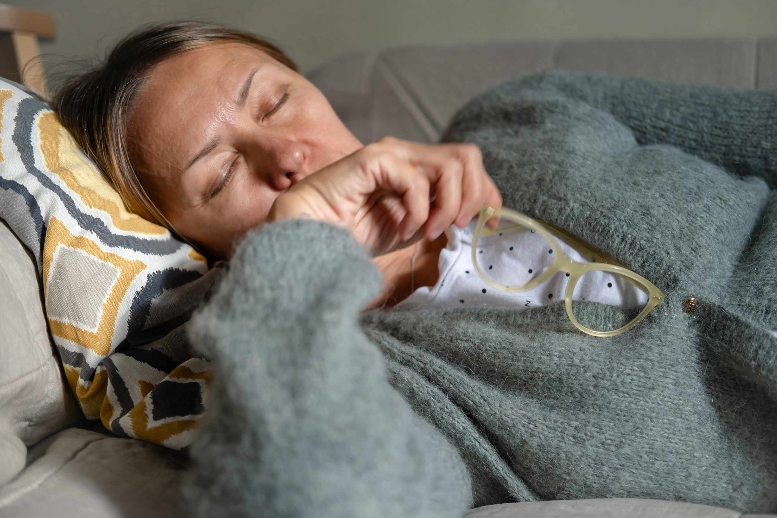 Woman resting under a blanket on a couch looking unwell, illustrating the fatigue, sleep disruption and immune vulnerability that can accompany perimenopause hormonal changes